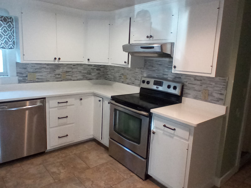 Gray mosaic backsplash and tan flooring installation in kitchen with stainless steel appliances and white cabinets